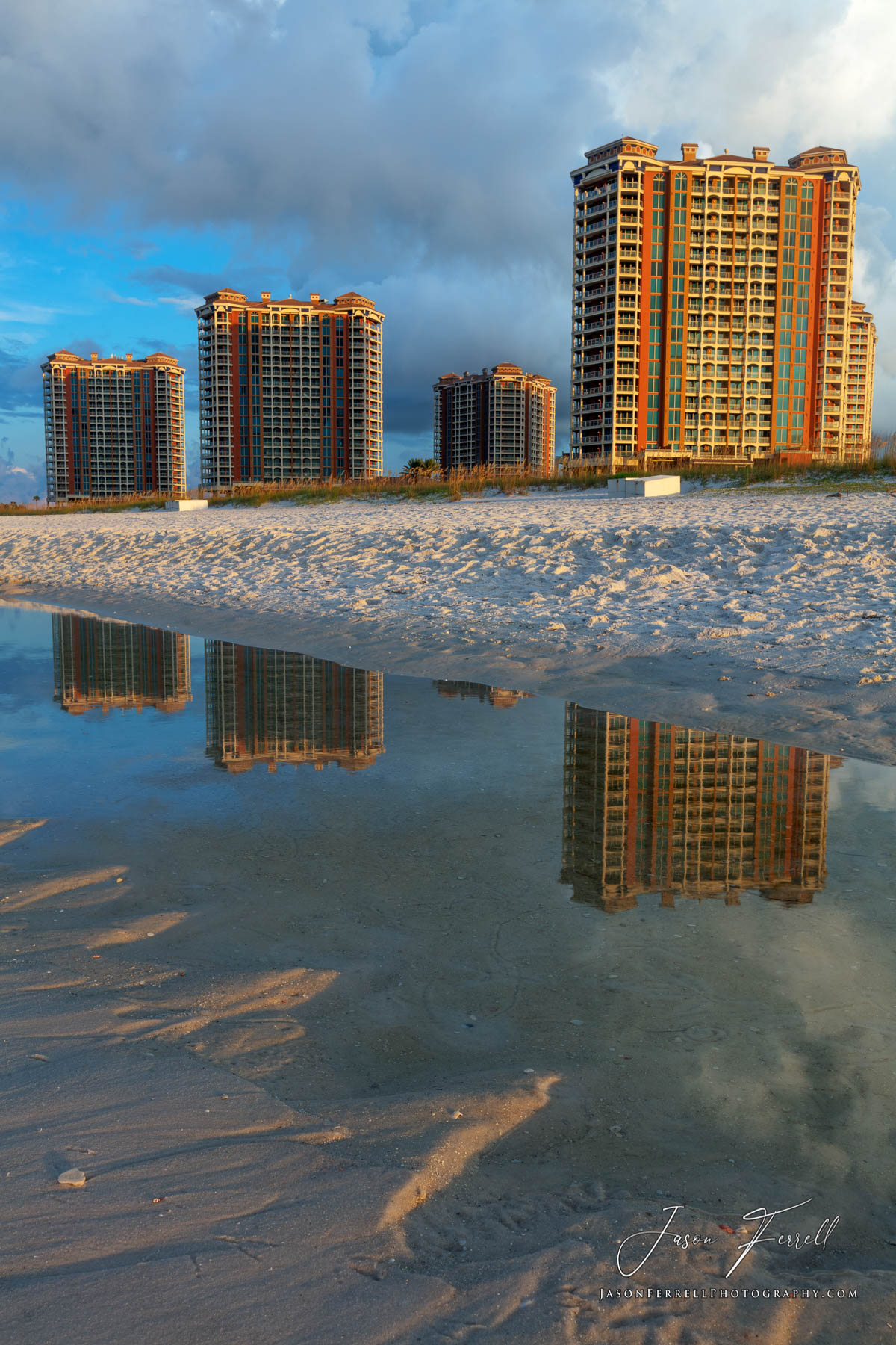 An early morning sunrise photo of the Portofino Island Resort Towers reflecting from a tidal pool on the beach.